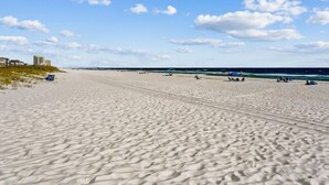 Una amplia playa de arena con algunas personas y sillas de playa, cielo despejado y una vista distante del océano.