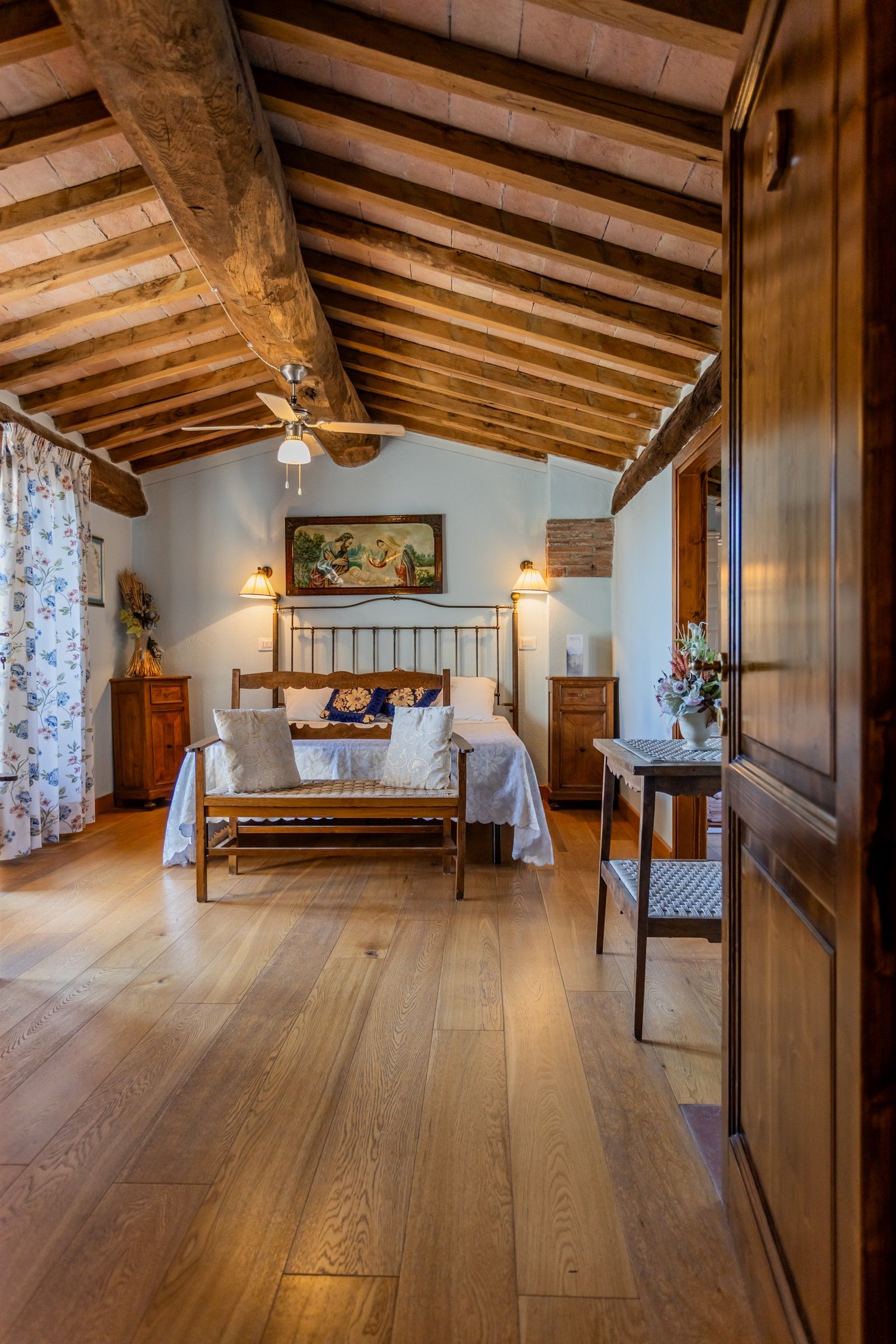 Une chambre avec un plafond en bois, un lit avec une tête de lit, une table de chevet, une table et une lampe fixée au mur.