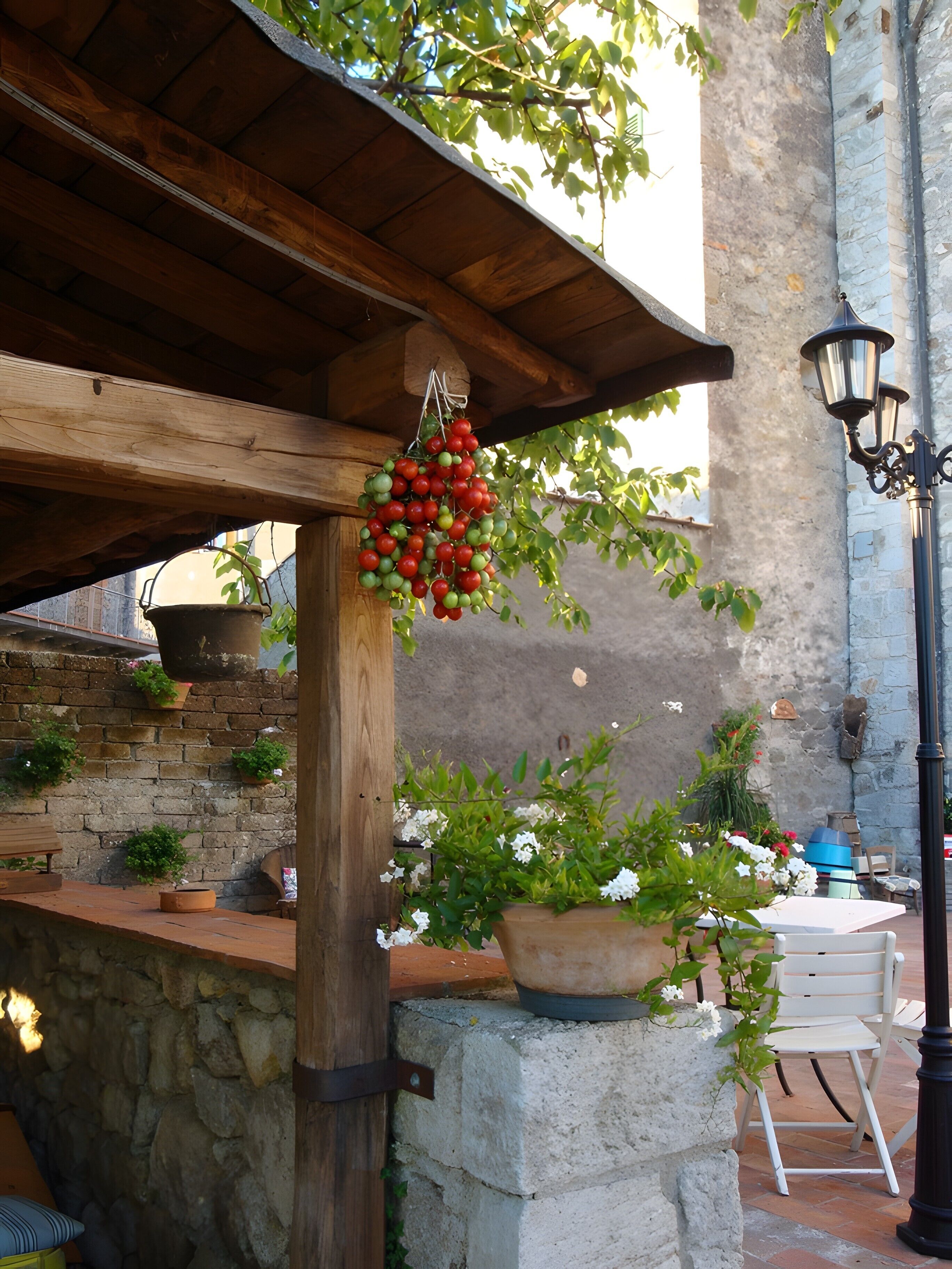 Ein rustikaler Sitzbereich im Freien mit einer Holzpergola, Steinmauern und Blumentöpfen.