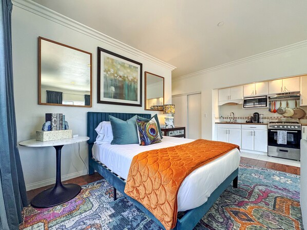 A hotel room with a bed, bedside table, and a kitchenette. - Saylors Aweigh Guest Suite (Seal Beach)