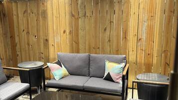 A covered outdoor seating area with a wooden bench, a sofa, and a table.
