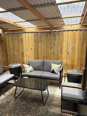 A covered outdoor seating area with a wooden bench, a sofa, and a table.