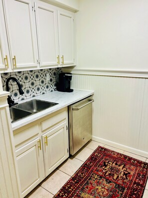 Una cocina con armarios blancos, un lavamanos de acero inoxidable, una cafetera y un salpicadero decorativo.