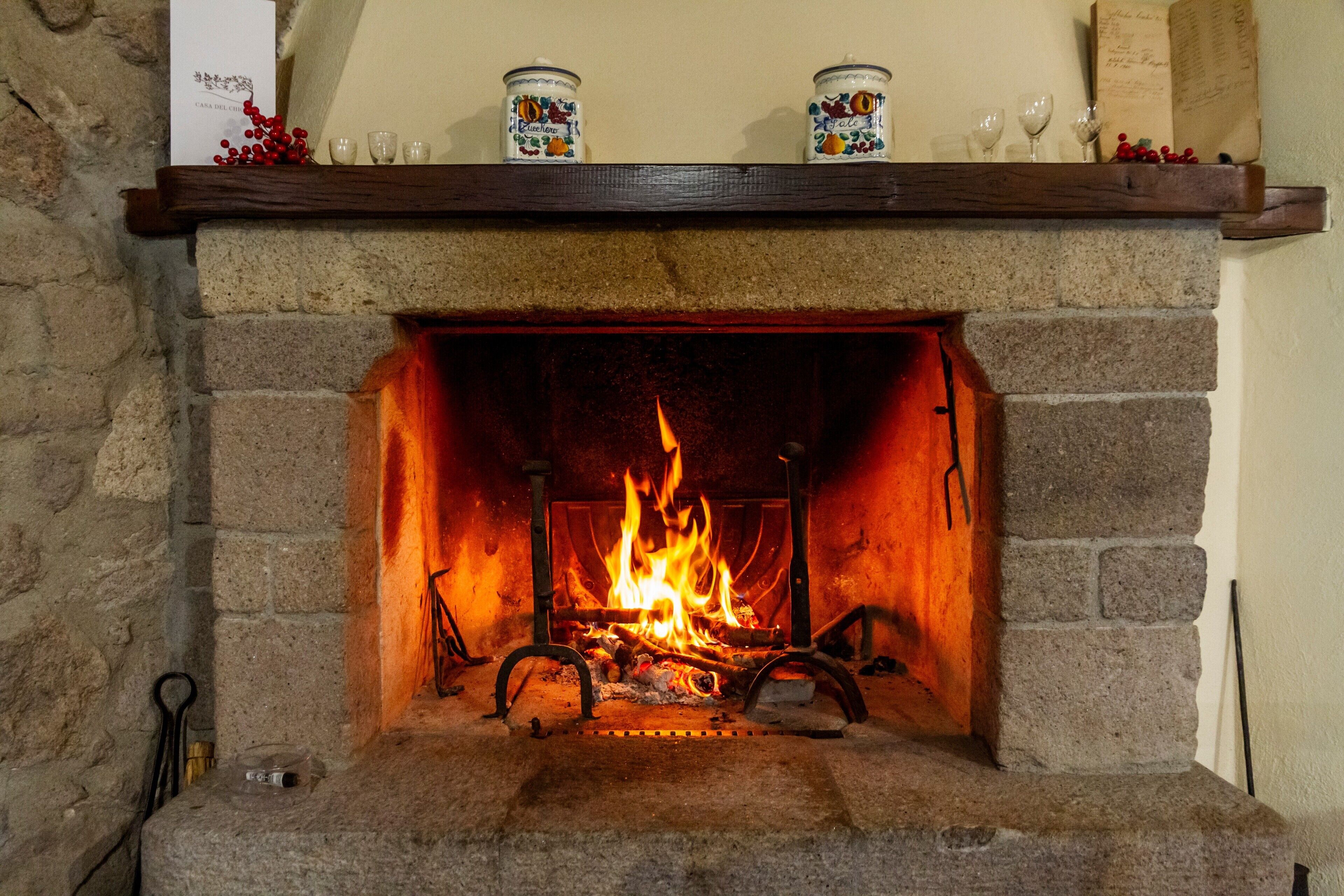 Ein Kamin aus Stein mit brennendem Feuer, eine Ablage darüber mit Dekoration, und ein Schild auf der linken Seite.