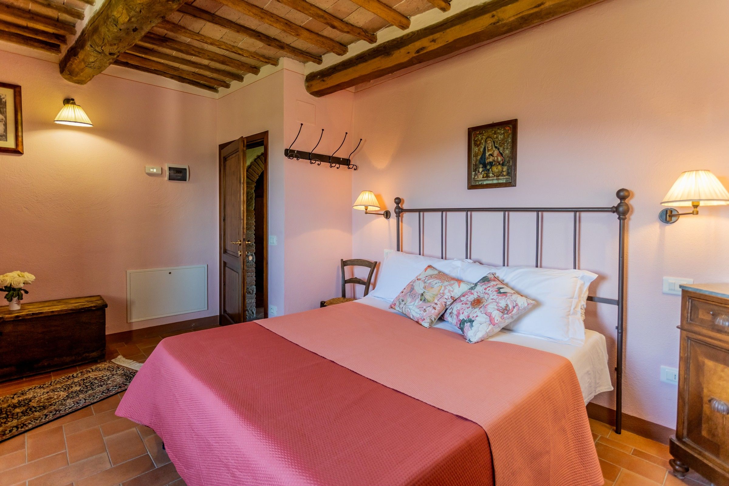 A bedroom with a bed, bedside lamps, a wooden headboard, a wall-mounted picture, and a door with a stone wall.