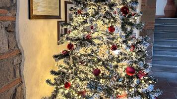 Ein festlich geschmückter Weihnachtsbaum mit Lichtern und Dekorationen vor einer Ziegelwand mit gerahmten Bildern.
