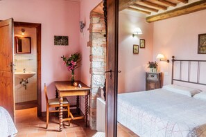 Une chambre à coucher avec un lit, une table en bois et une chaise, une petite table de chevet avec une lampe, et un mur en briques.