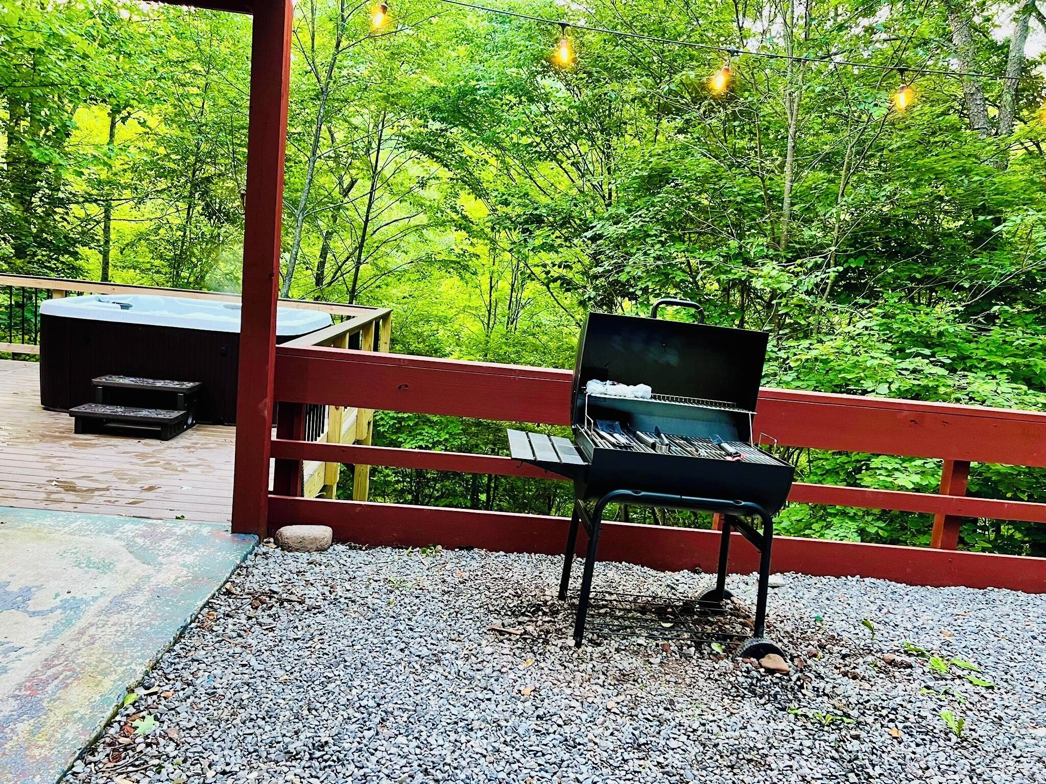 Un barbecue avec une table en bois et un jacuzzi sur une terrasse entourée de verdure.
