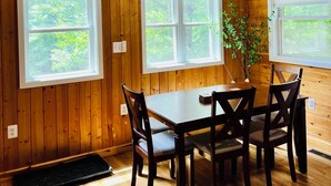 A wooden-paneled room with a dining table and chairs, large windows, and a chandelier.