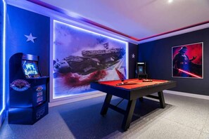 A pool table with a Star Wars-themed wall art, a gaming console, and a poster of Darth Vader.