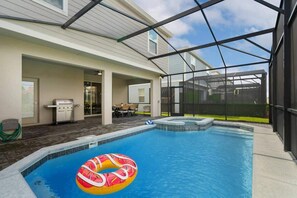 A swimming pool with a hot tub, a grill, and a covered patio area.