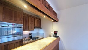 A modern kitchen with wooden cabinets, a stainless steel oven, a coffee maker, and a tiled backsplash.