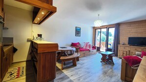 A spacious living area with a wooden staircase, a dining table, a sofa, and a television.