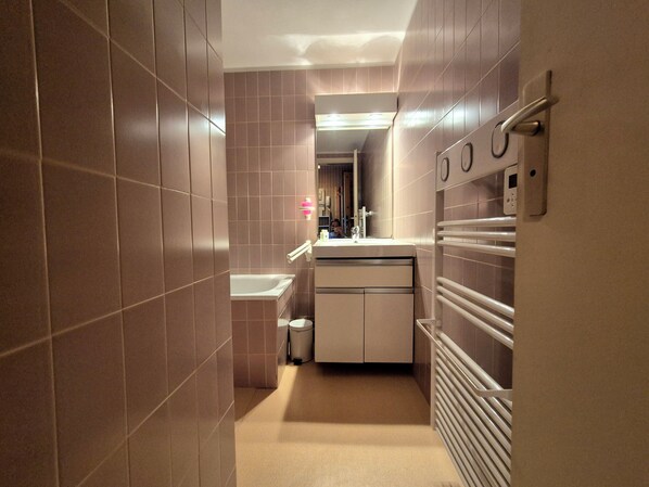 Et smalt, moderne badeværelse med badekar, toilet og håndvask.
