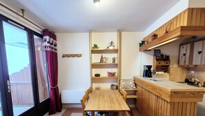 A cozy kitchen with a wooden table and chairs, a built-in bookshelf, and a coffee station.