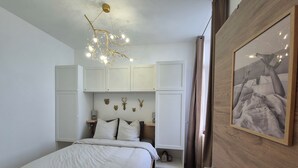 Une chambre à coucher avec un lit, des armoires blanches, un luminaire fixé au mur et un tableau encadré.