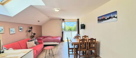 Una habitación acogedora con cama, sofá rojo, mesa de comedor con sillas, televisor y lámpara de techo.