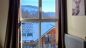 Ein Zimmer mit einem großen Fenster, das Blick auf eine verschneite Berglandschaft und eine Holzhütte bietet.