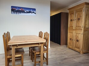 A wooden dining table with six chairs, a wooden cabinet with multiple doors, and a wall-mounted picture of a snowy mountain scene. - Appartement spacieux Au Petit Bois, La Féclaz (La Feclaz)