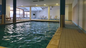 Ein hallenbad mit klarem Wasser, einer sonnendurchfluteten Decke und Liegestühlen am Beckenrand.