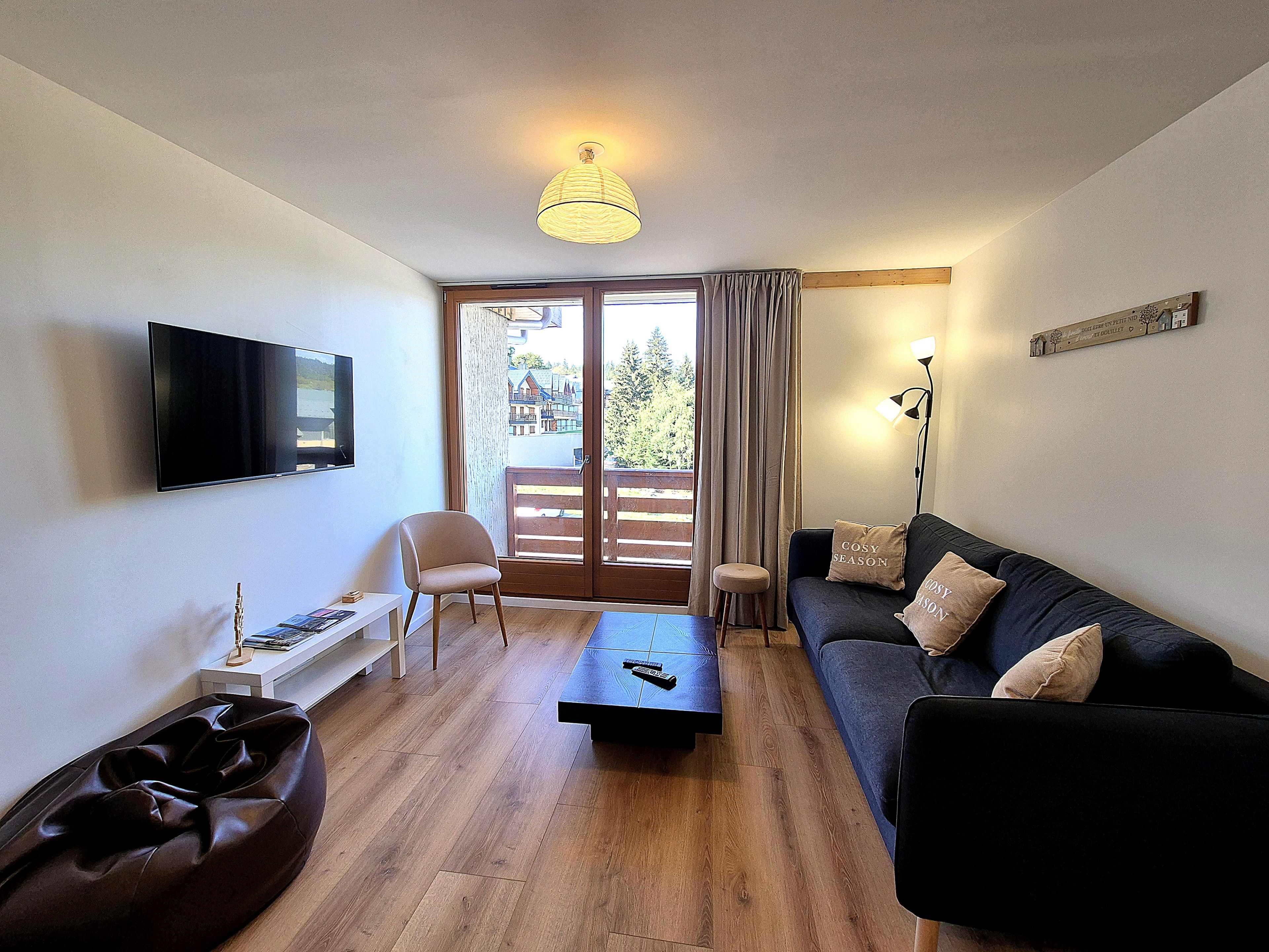 Un salon moderne avec un téléviseur à écran plat, un canapé avec des coussins, une table basse, un fauteuil et un plancher en bois.