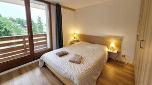 A bedroom with a large bed, wooden headboard, two bedside lamps, and a view of greenery through a sliding door.