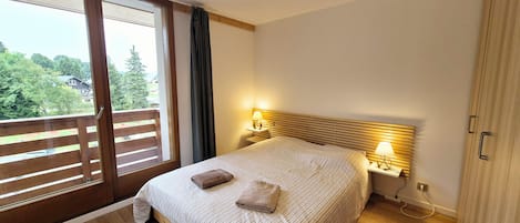 A bedroom with a large bed, wooden headboard, two bedside lamps, and a view of greenery through a sliding door.