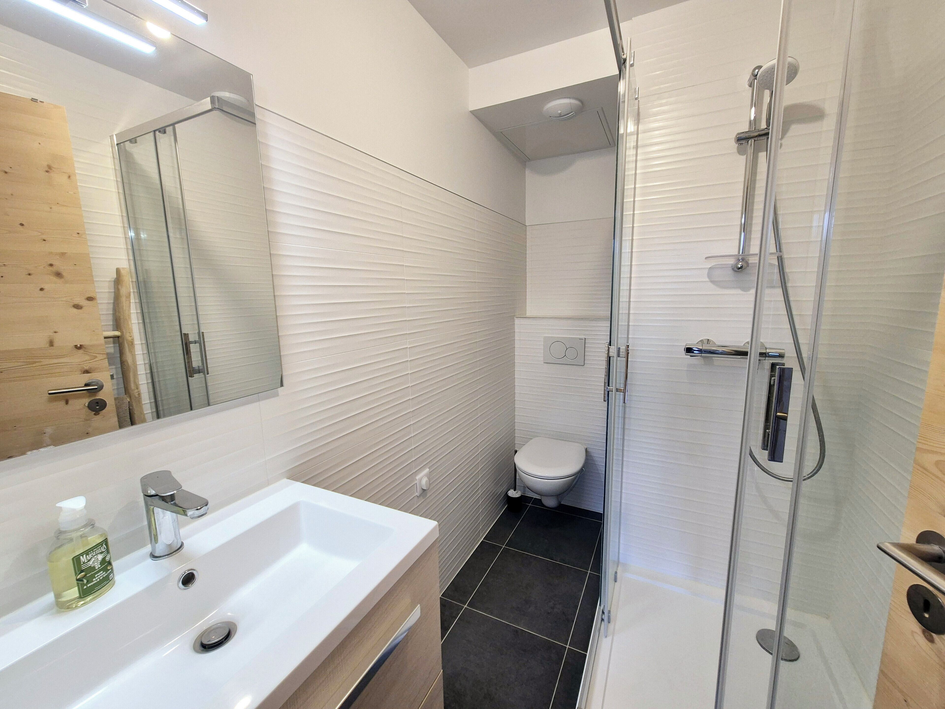 Un baño moderno con lavamanos blanco, cabina de ducha de vidrio y un inodoro.