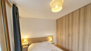 A bedroom with a bed, bedside lamps, a wooden wardrobe, and a ceiling light.