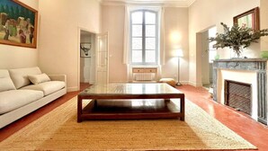A living room with a glass-top coffee table, a beige sofa, a fireplace, and a large window. - Hôtel Boudon 4, Luxury 1BR in Écusson (Nîmes)