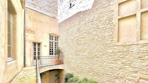 A narrow alleyway with a stone wall, a small balcony with a metal railing, and a potted plant on the ground. - Hôtel Boudon 4, Luxury 1BR in Écusson (Nîmes)