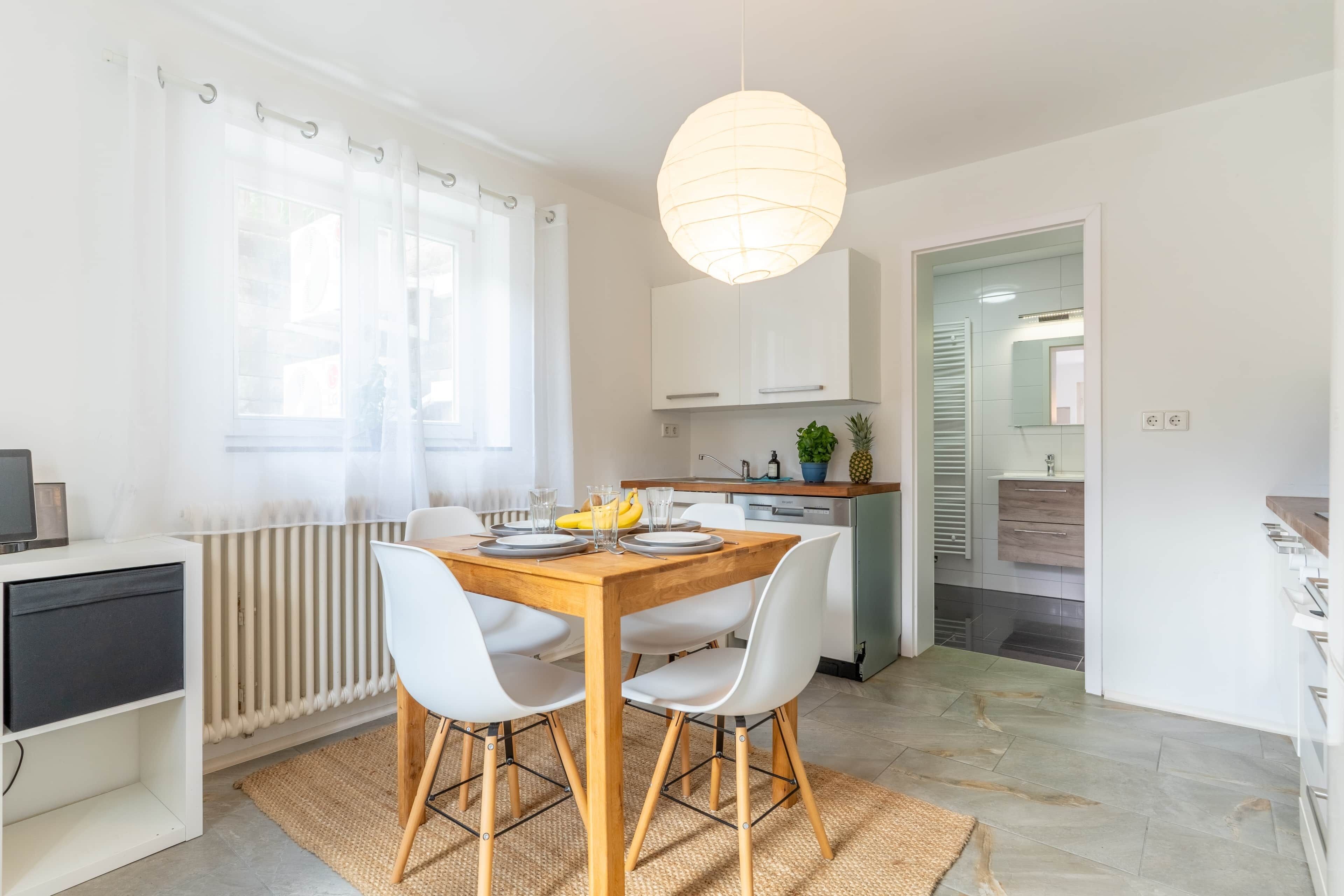 A modern kitchen with white cabinets, a wooden dining table, and a hanging light fixture.