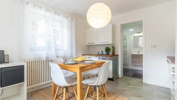 A modern kitchen with white cabinets, a wooden dining table, and a hanging light fixture.