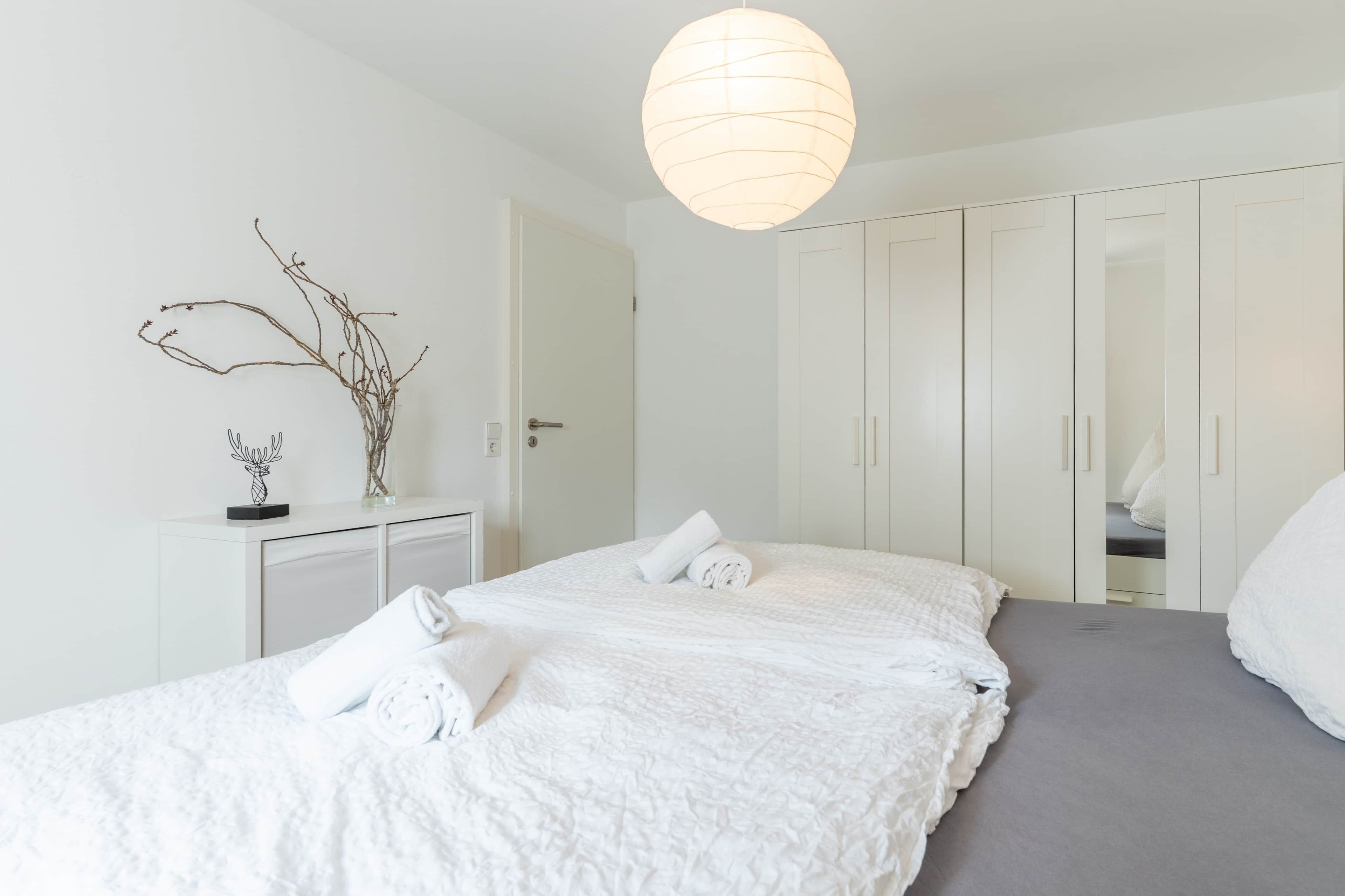 A hotel room with a large bed, a desk with a vase, and a wardrobe.