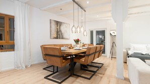 Un espace repas moderne avec une table en bois et des chaises en cuir, un luminaire suspendu et un tableau au mur.