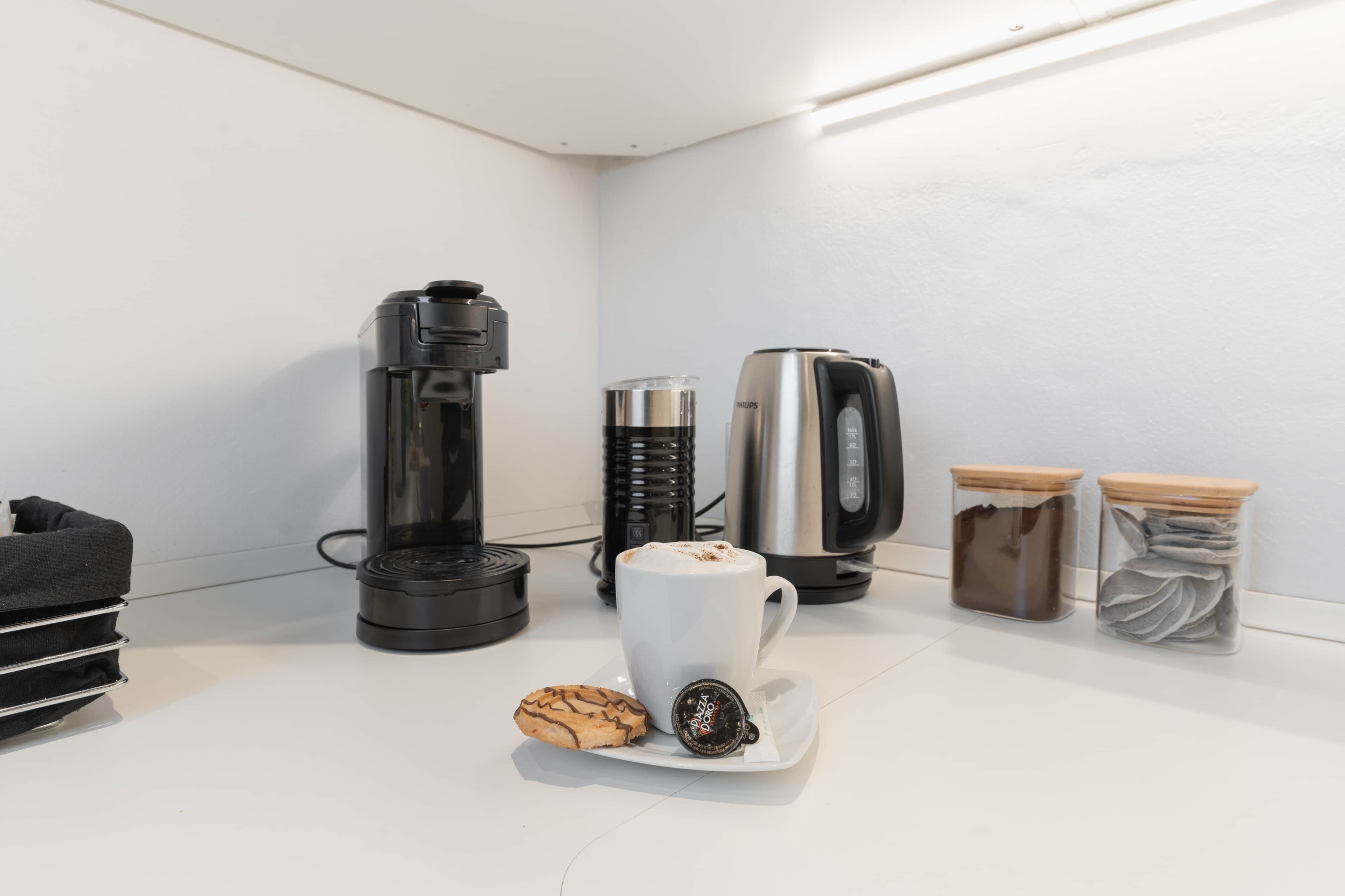 Un coin café comprenant une machine à café, une tasse, une pâtisserie et deux bocaux de grains de café.