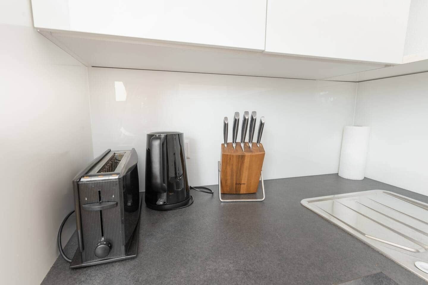 Eine Küchenzeile mit Toaster, Kaffeemaschine, einem Messerblock und einem Papierhandtuchspender.