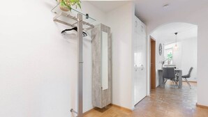 A hallway with a wooden floor, a glass shelf with a plant, a wardrobe, and a dining area with chairs and a table. - Untersee Suite | Lake nearby – Terrace - Workspace (Radolfzell)