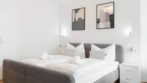 A modern bedroom with a grey upholstered bed, white bedding, and two framed artworks on the wall. - Untersee Suite | Lake nearby – Terrace - Workspace (Radolfzell)