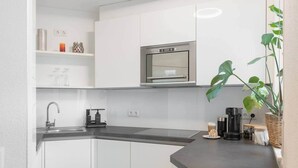 A modern kitchen with white cabinets, a stainless steel refrigerator, a coffee machine, and a potted plant. - Untersee Suite | Lake nearby – Terrace - Workspace (Radolfzell)