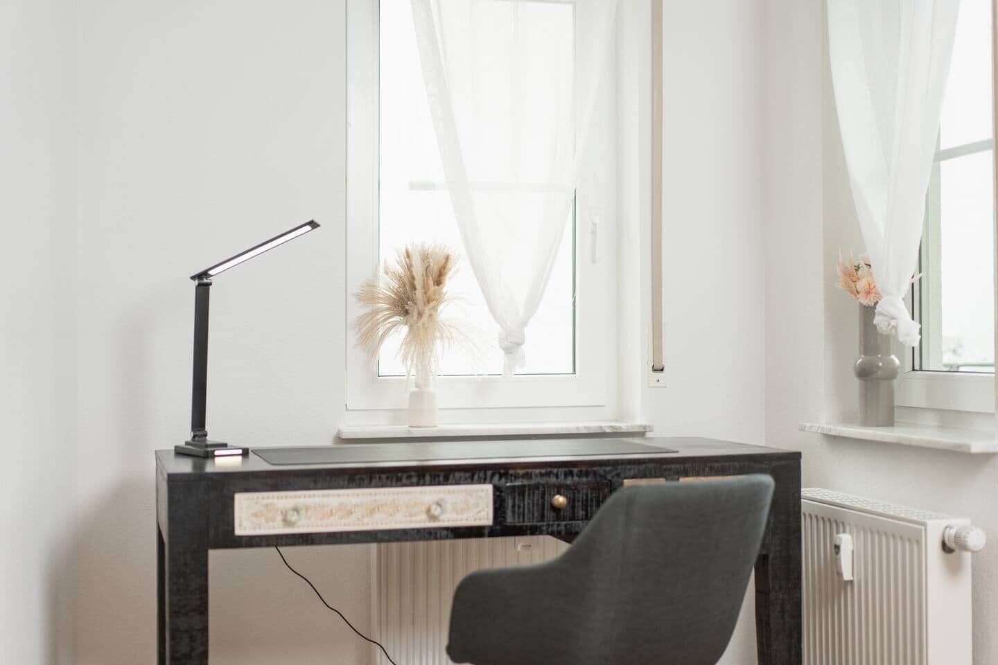 Ein moderner Arbeitsplatz mit Schreibtisch, Stuhl und Fenster mit leichtem Vorhang.