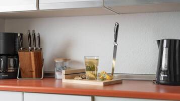 Una encimera de cocina con una cafetera, un cuchillo, un vaso de té y un bloque de madera con rodajas de limón.