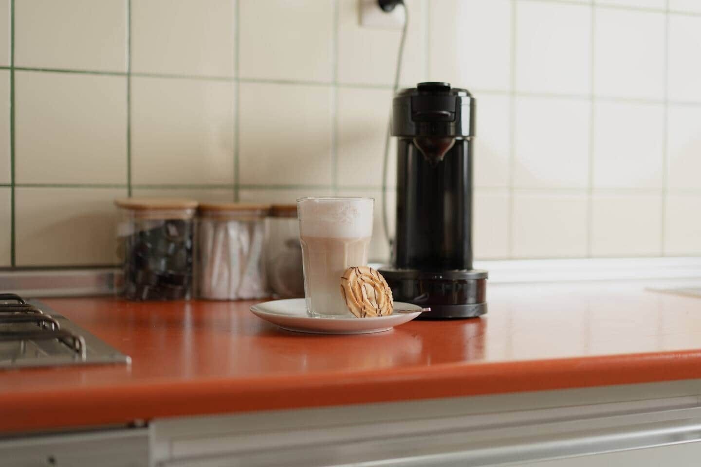 A kitchen counter with a coffee maker, a glass of milk, and a pastry.