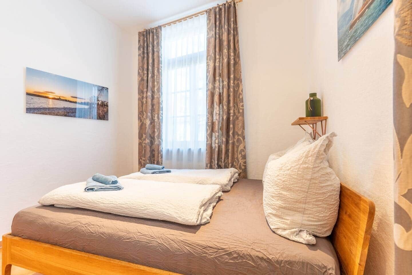 A bedroom with a bed, pillows, a small table with bottles, and a painting on the wall.