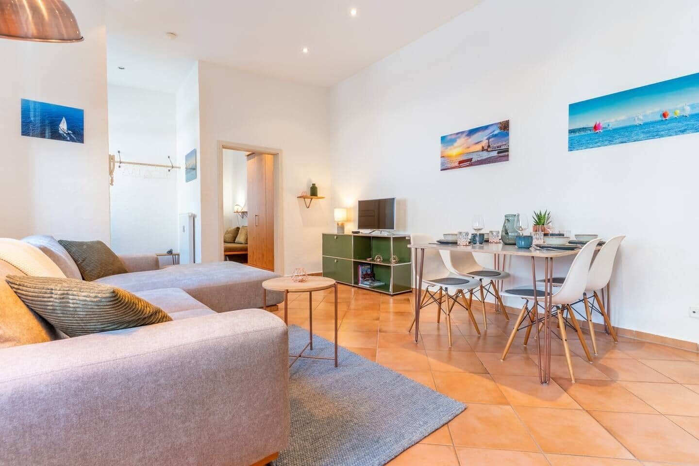 Un salon moderne avec un canapé, une table à manger et des chaises, ainsi qu’un téléviseur posé sur un meuble.