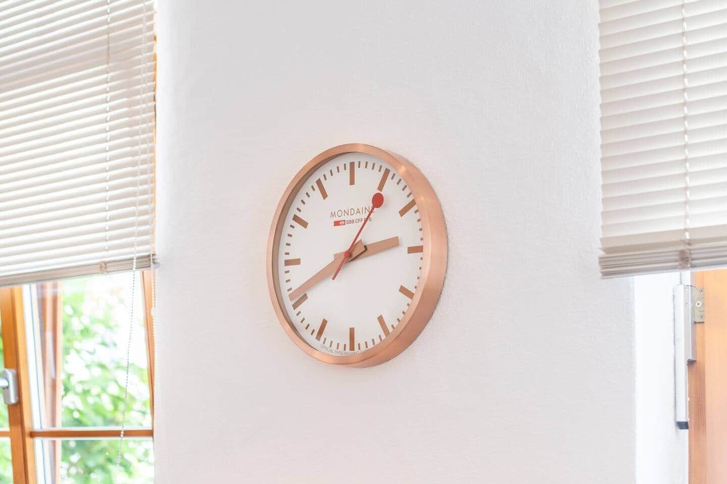 A round wall clock with a white face and rose gold frame, mounted on a white wall.