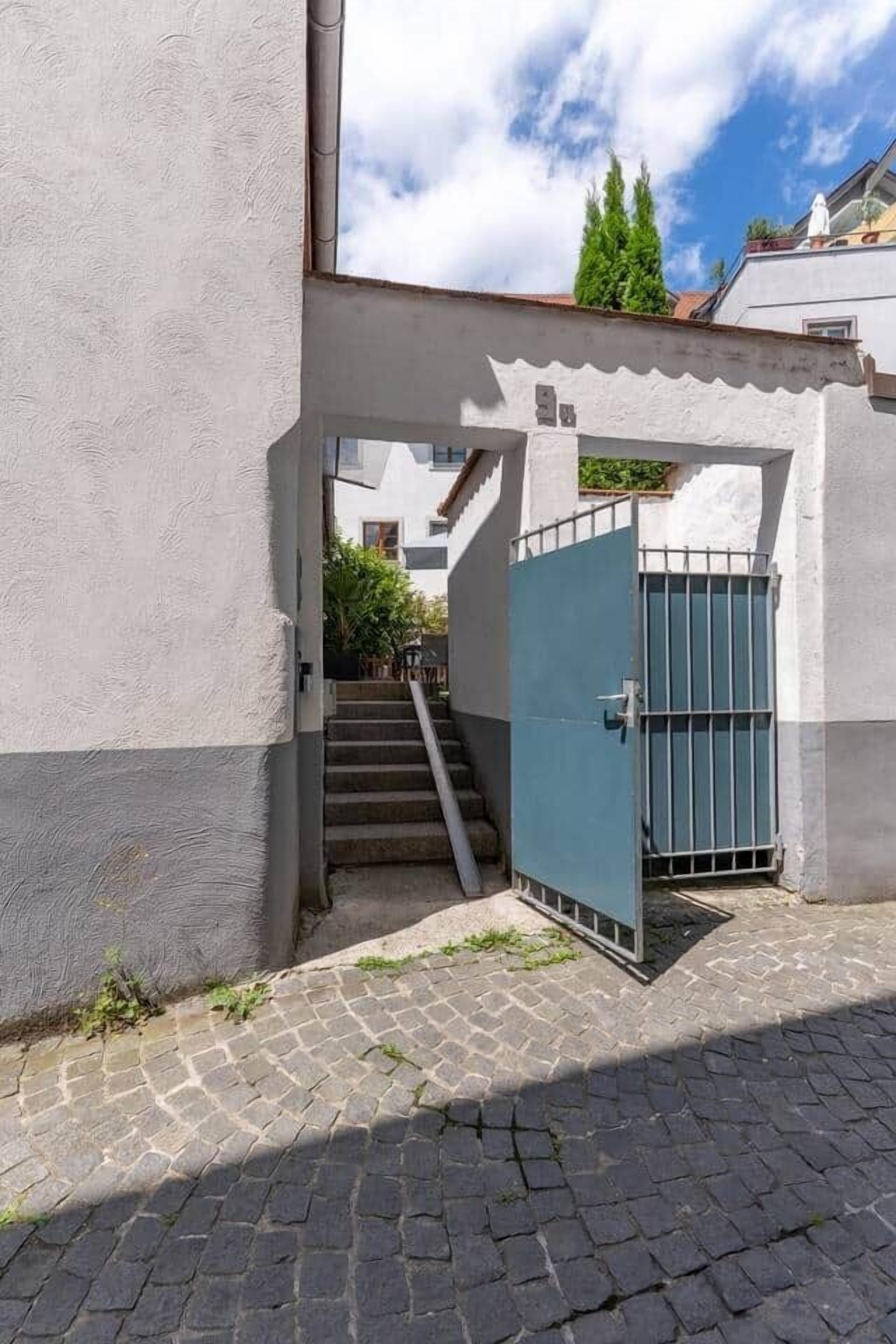 A narrow alleyway with a blue gate, cobblestone pavement, and a staircase leading to a building.