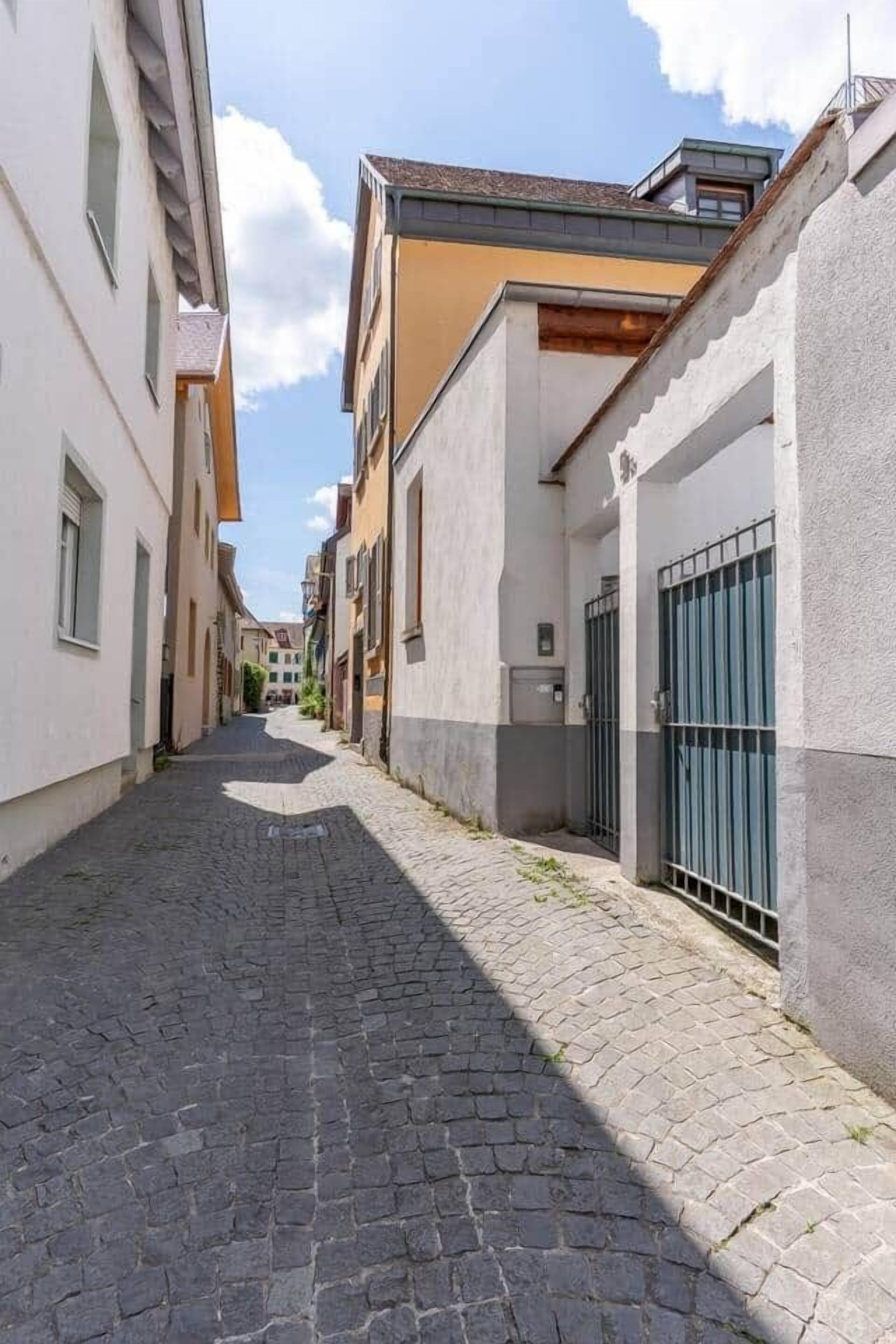 Una estrecha calle adoquinada flanqueada por edificios con balcones y una entrada porticada.