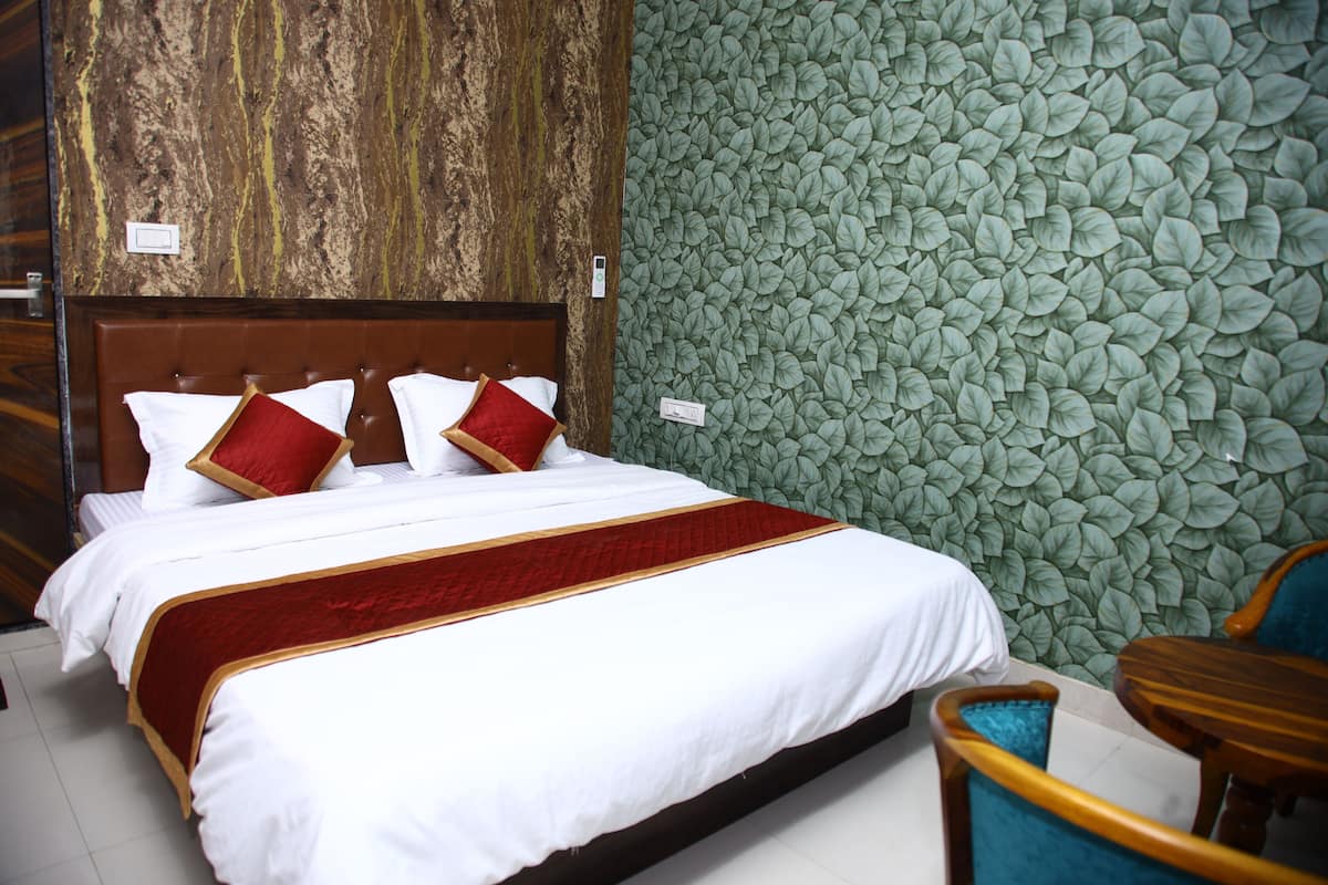 A neatly made bed with white bedding and red accents, a wooden headboard, and a green leaf-patterned wall.