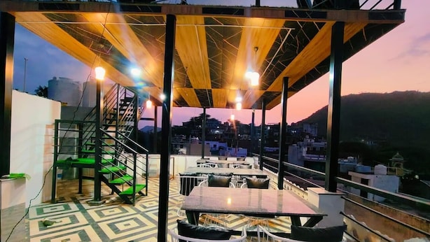 An outdoor terrace with tables and chairs, a staircase, and a view of the cityscape at dusk. - Hotel L S Restaurant & Spa (Udaipur)
